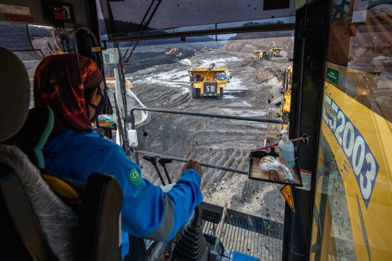 在印度尼西亚的一个煤矿里，一台挖掘机正等待在一辆自卸卡车里