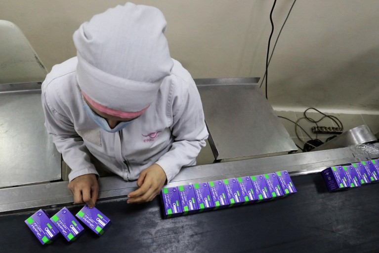 A lab technician wearing a face mask and a protective suit works on a production line packaging Molnupiravir