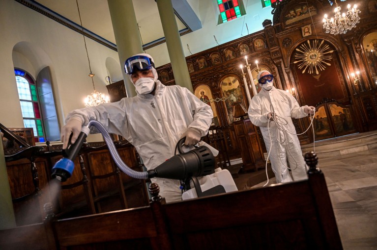 Workers in masks and overalls spray disinfectant on the pews of an Orthodox Greek Church in Istanbul