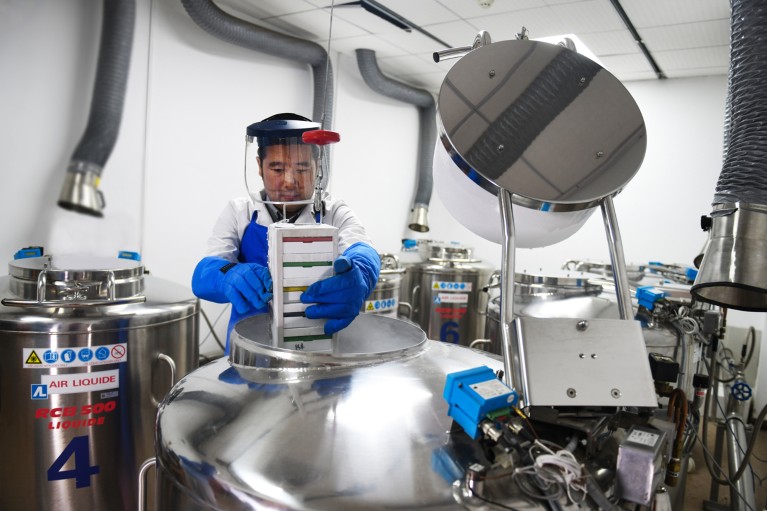 Lin Liang wearing a protective visor, overalls and think gloves lifts seed samples from a cyrogenic storage tank