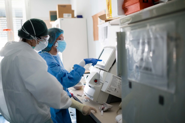 Two nurses in PPE check medical records on a computer in a COVID ward