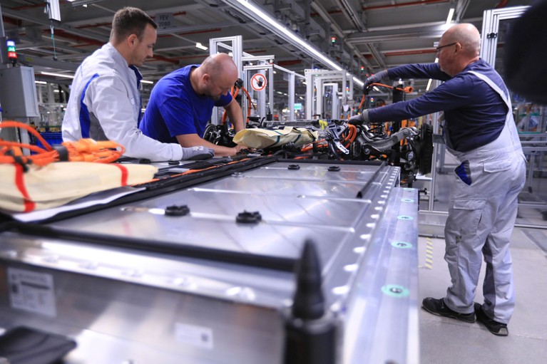 Employees connect a lithium-ion battery pack to an electric motor on a car assembly line