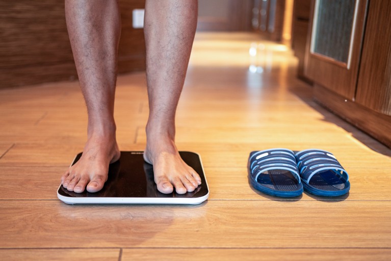 Close up of a man in bare feet standing on a weighing scale next to some sandals