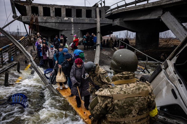 Soldiers help evacuees cross a destroyed bridge as they flee the city of Irpin during the invasion of Ukraine