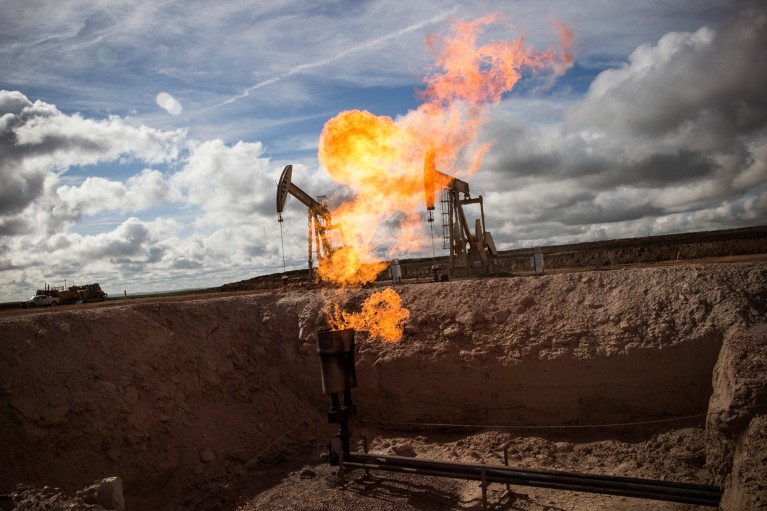 A gas flare is seen in the centre of the frame at an oil well site