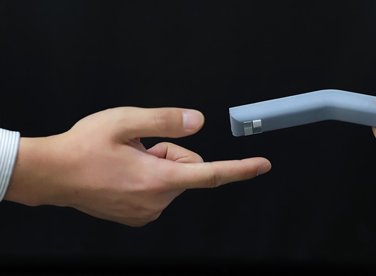 A pointed finger reaches out to touch the artificial tactile perception smart finger with a black background