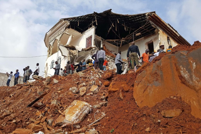 Vista de ángulo bajo de personas reunidas en un edificio dañado en un sitio de deslizamiento de tierra en Freetown, Sierra Leona