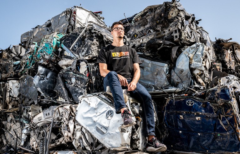 Gianluca Torta sits in a junk yard on a pile of crushed cars.
