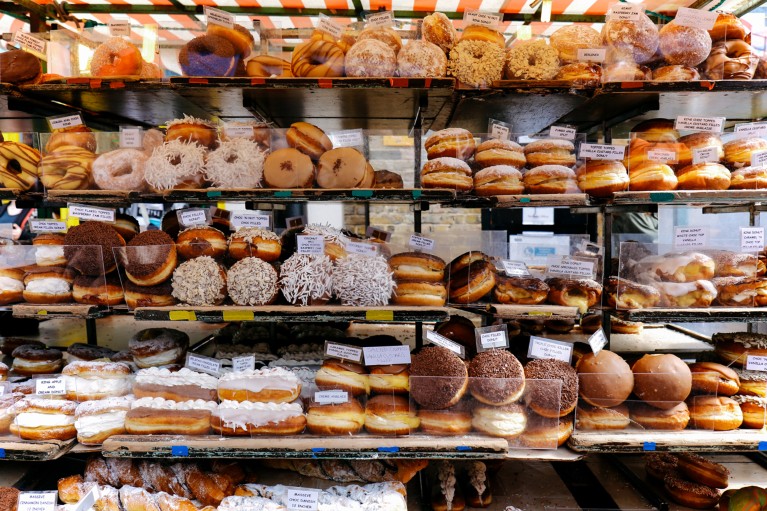 Shelves piled high with a variety of doughnuts for sale at a market.