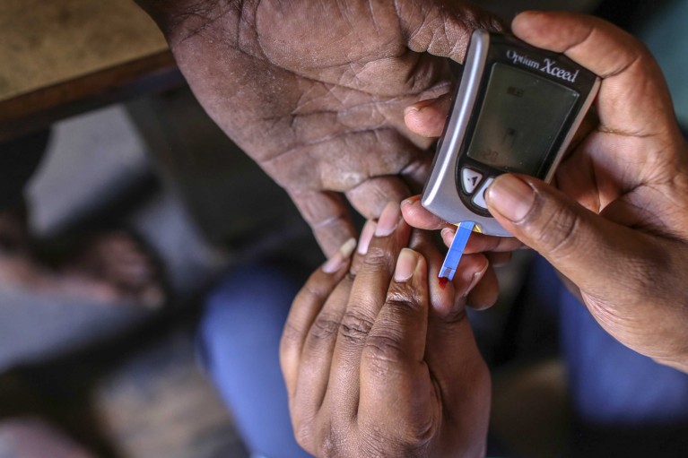 Close up on the hands of a medical worker using a glucometer to check the blood glucose level of a patient.