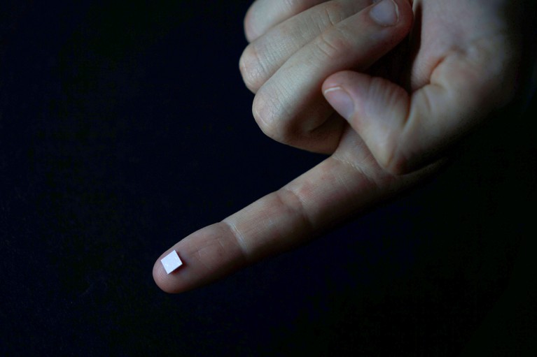 A tiny on-chip spectrometer sitting on a fingertip with a black background
