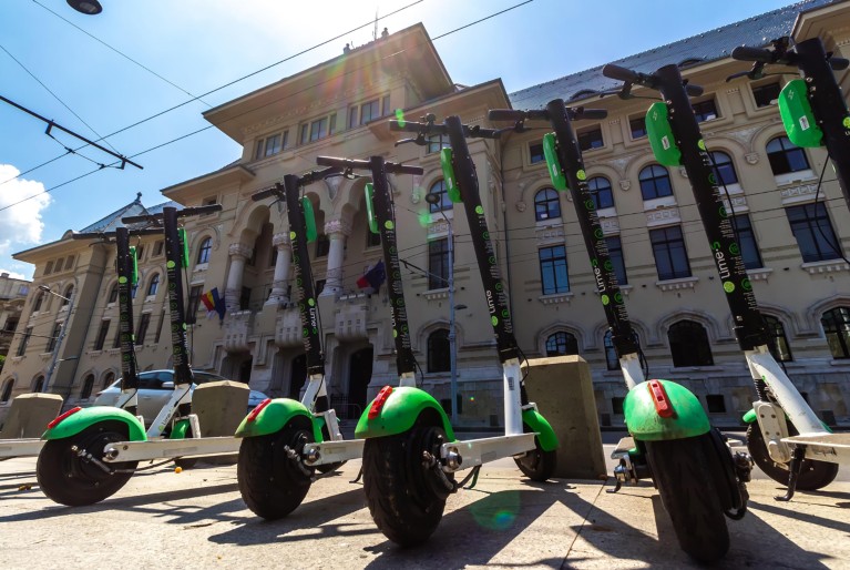 Low-angle view of a row of Lime-S Electric Scooters parked on a pavement.