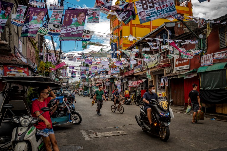 Men are pictured on a street filled with campaign posters in Manila, Philippines