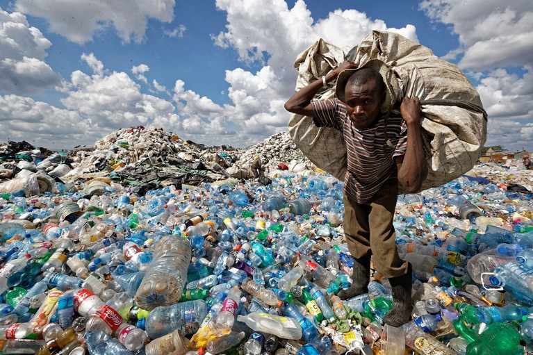 A man walks on a mountain of plastic bottles as he carries a sack of them at the dump in Nairobi, Kenya.