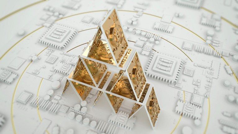A house of cards built from gold bitcoin tokens sits on top of a circuit board