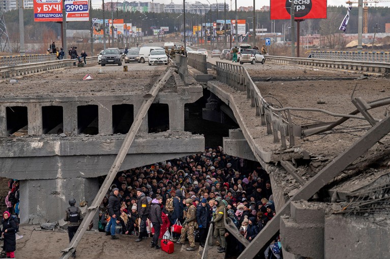 Ukrainians crowd under a destroyed bridge as they try to flee across the Irpin River in the outskirts of Kyiv, Ukraine