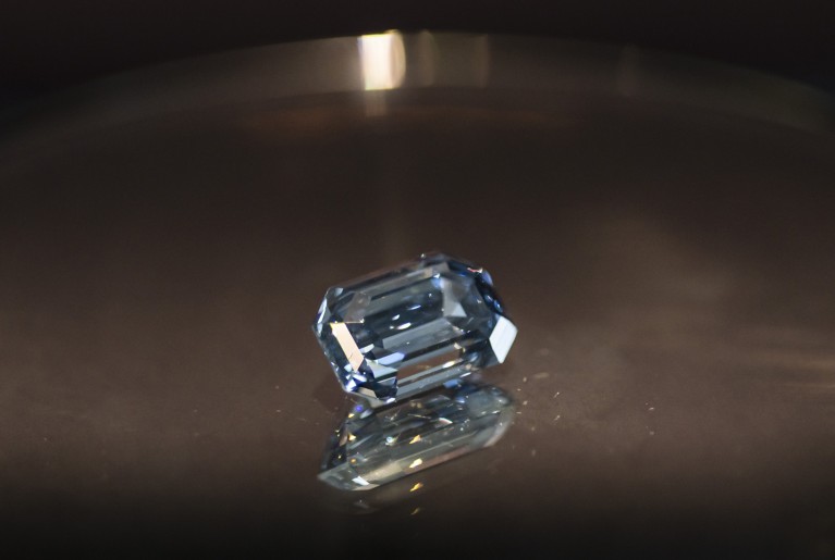 A close-up view of the 'De Beers Cullinan Blue' diamond on a dark grey reflective surface