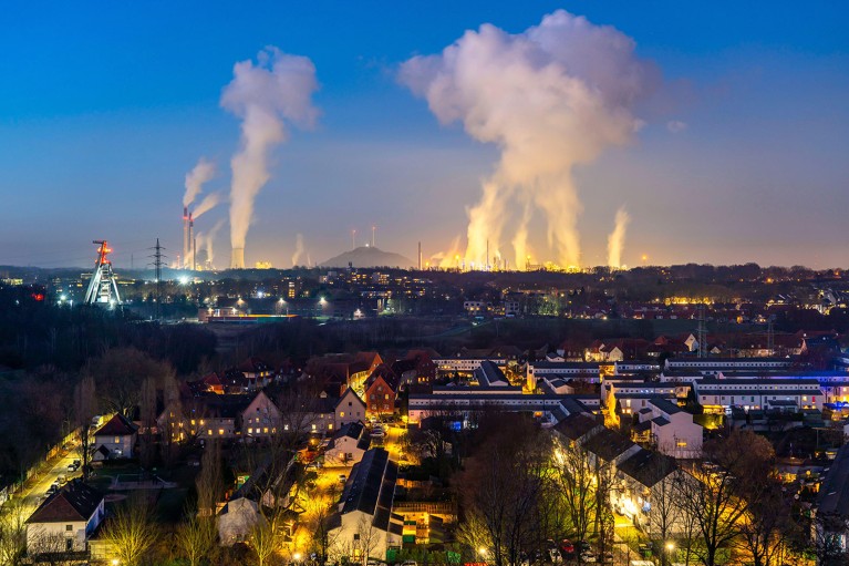 Modern industrial landscape showing emissions from a coal fired power station, oil refinery and coal mine, illuminated at night