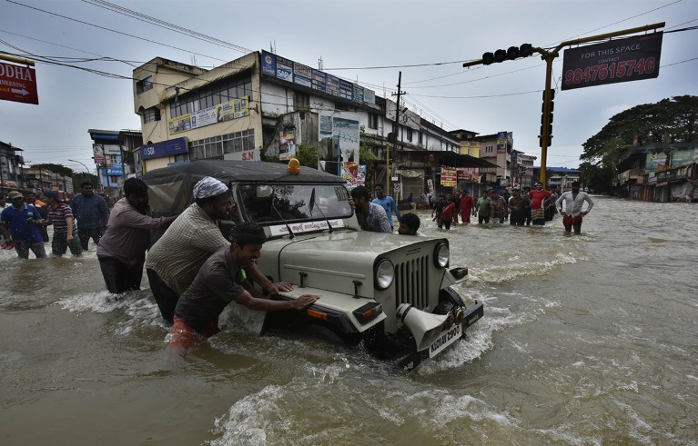 People push vehicles stuck in the flood water at Panadala in district Pathanamthitta, India.