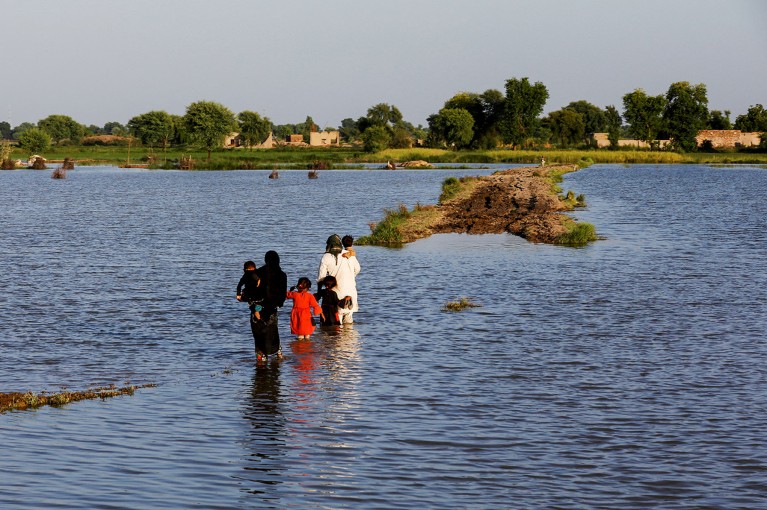 A family walks amid flood waters following rains and floods during the monsoon season in Mehar, Pakistan