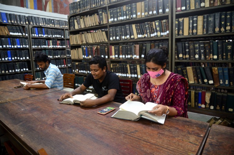 Two male and one female students read books at a table in a library