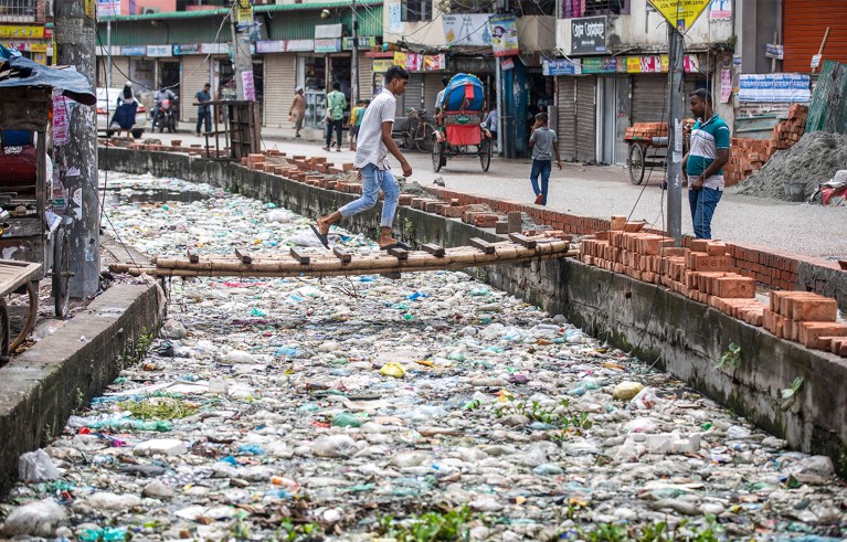 Man walks through a canal which is blocked by piles of plastic waste and food waste dumped, Bangladesh, Dhaka.