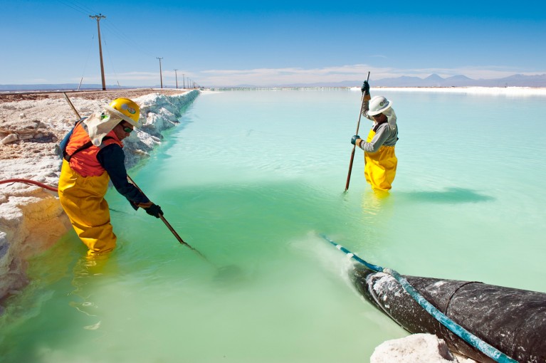 Two workers wearing yellow overalls in a lithium evaporation pond in the Atacama desert, Chile