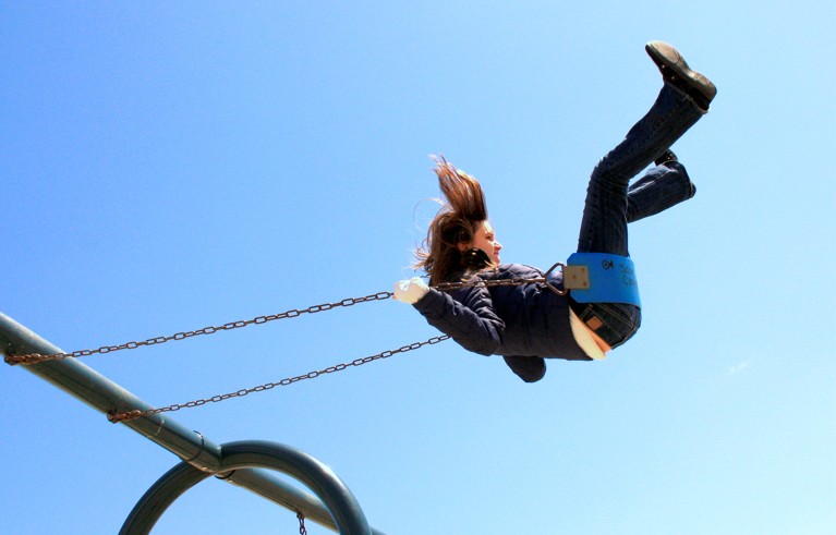 A young female play hard in the swing with a blue sky at her background.