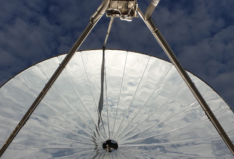 Part of a reflective dish with reactor apparatus framed against the sky.