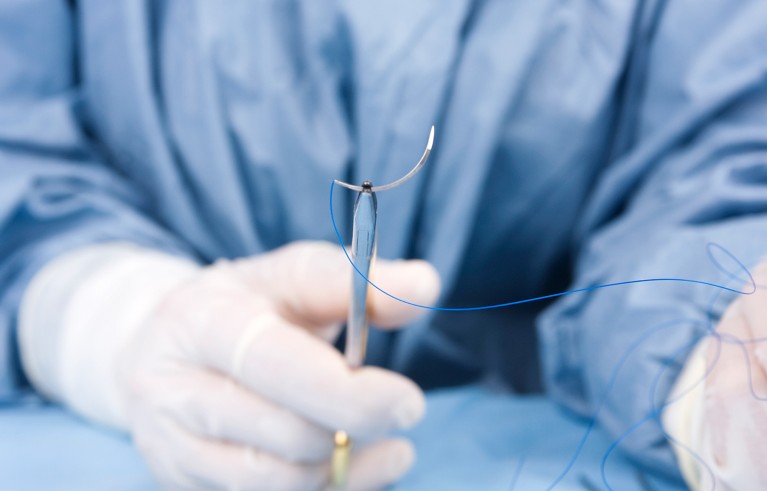 Doctor holding surgical stitch by scissors during plastic surgery operation.