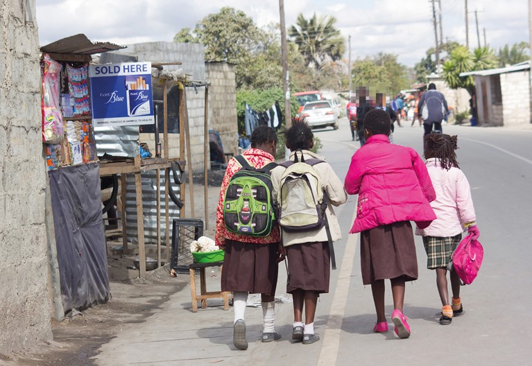 Four school children walking past a stall selling cigarettes on the side of the road.