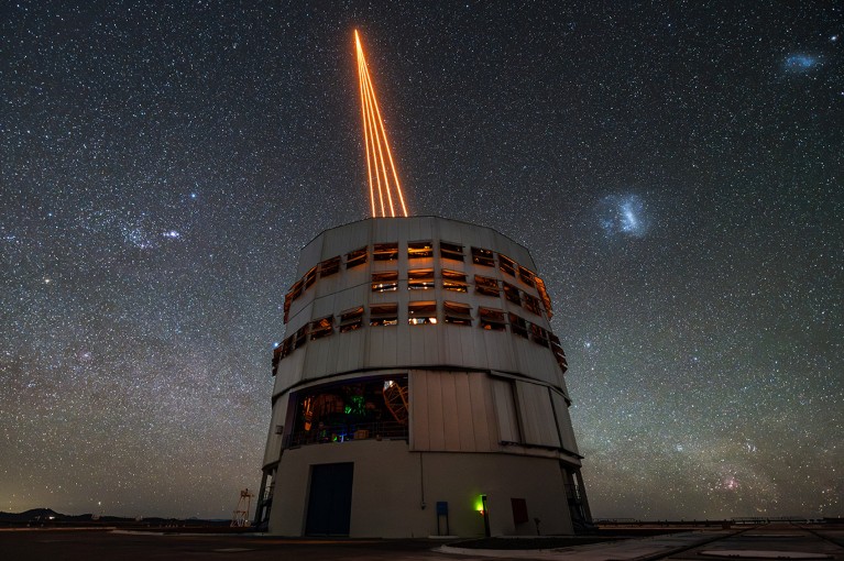 An observatory building emitting four orange laser beams that converge to a point, against a starry sky.