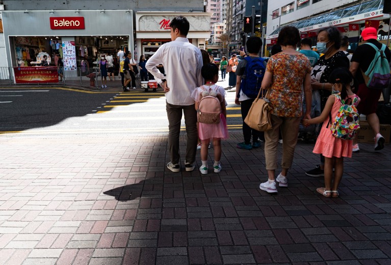 Rear-view of pedestrians standing in the shade as they wait to cross a street