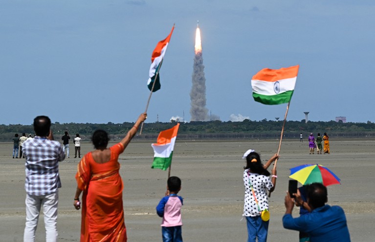 People wave Indian flags as a rocket launches.