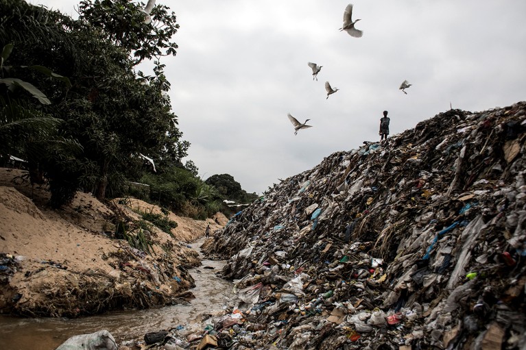 A young girl stands on a dirty river bank littered with garbage in the Ngaliema neighborhood in Kinshasa.