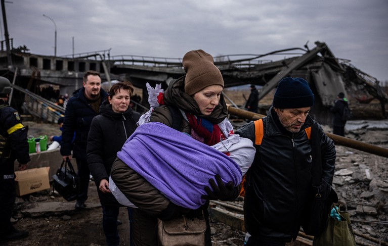 A woman carrying her baby crosses a destroyed bridge with other people.
