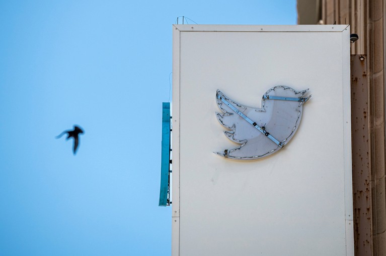 A partially removed sign at Twitter headquarters in San Francisco, California with a distant bird flying across the sky