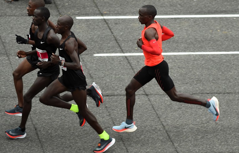 Three runners wearing black, in a line in front of one runner wearing bright orange