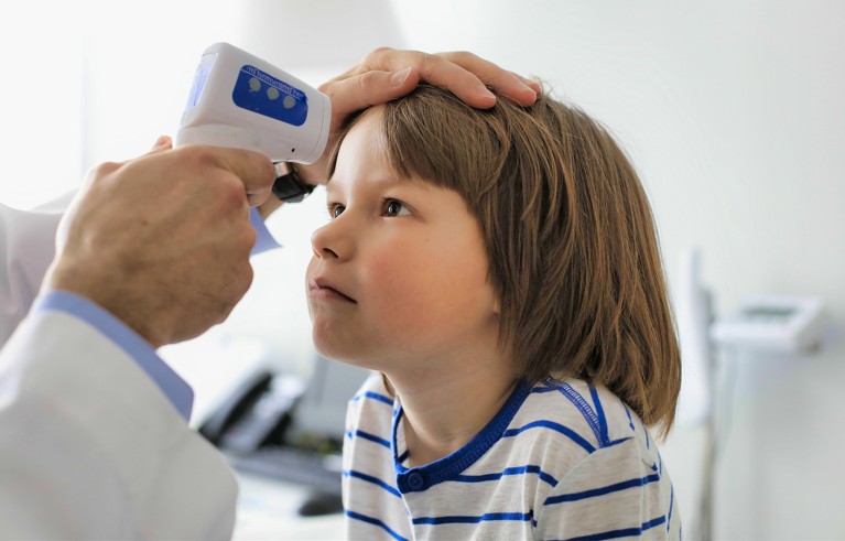 Cropped image of doctor measuring temperature of boy with infrared thermometer at hospital.
