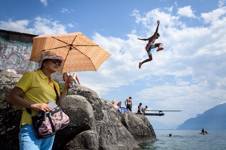 A boy jumps into Geneva Lake while an older woman shields herself from the sun with an umbrella