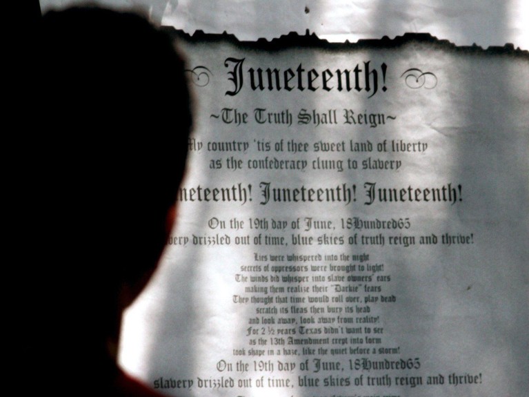 The silhouetted back of a person's head looking at a poster for Juneteenth.