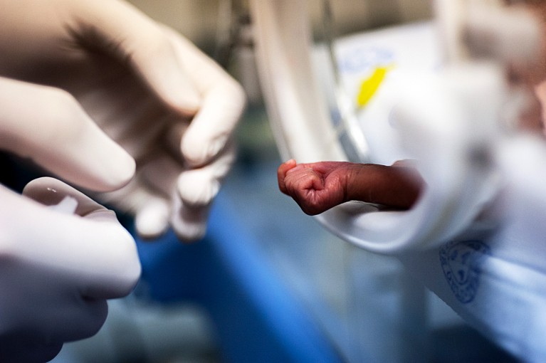 Close-up of a tiny premature baby hand reaching out of an incubator