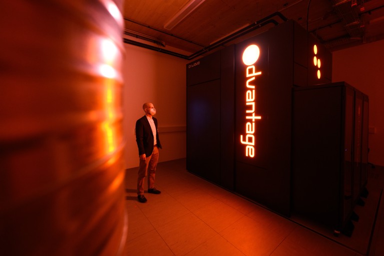 An employee stands next to the D-Wave Systems Advantage quantum computer, lit only by an orange glow