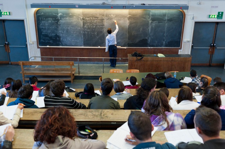 A teacher writes on a chalkboard during a lecture with students