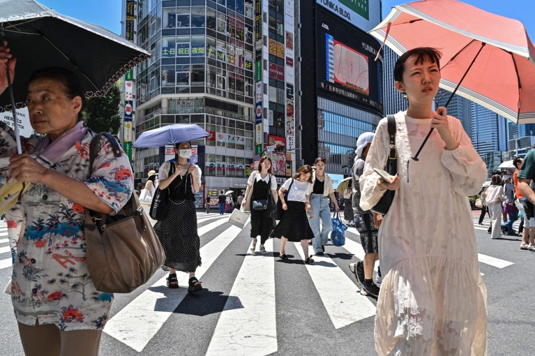 People use umbrellas and parasols to seek relief from the heat while crossing a street in Tokyo