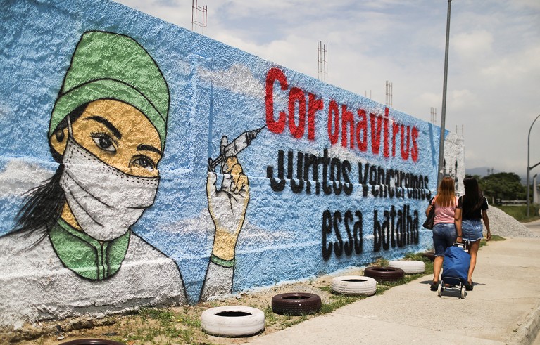 People walk past a graffiti amidst the spread of COVID-19 in Rio de Janeiro. The graffiti reads: "Coronavirus, together we will win that battle".