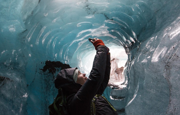 A glaciologist and climate change scientist photographs inside a moulin, an ice cave, Skaftafell glacier, Vatnajokull National Park. Iceland.