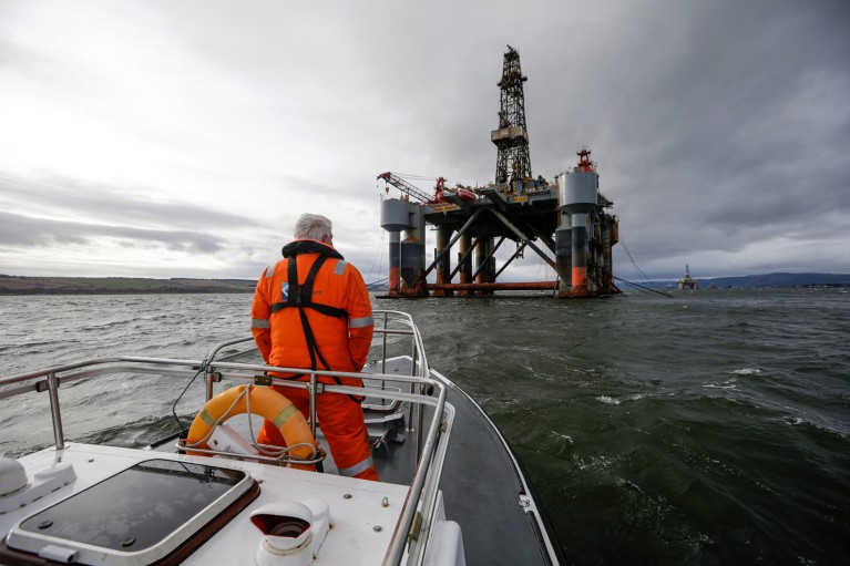 A man in orange hi-vis clothing stands on the deck of a pilot boat, looking out to the Ocean Princess oil platform