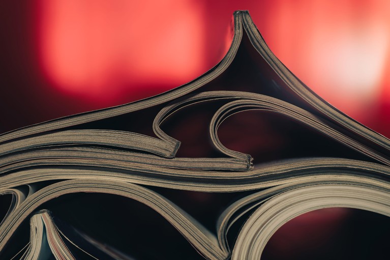 A close up view of journal magazines that have been folded open and piled together against a red background.