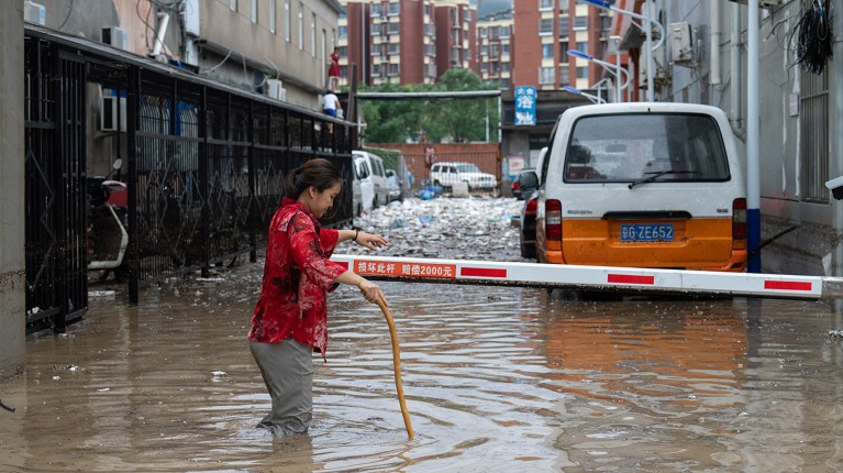 A woman walks with a stick through a flooded street in Mengtougou district on July 31, 2023 in Beijing, China.
